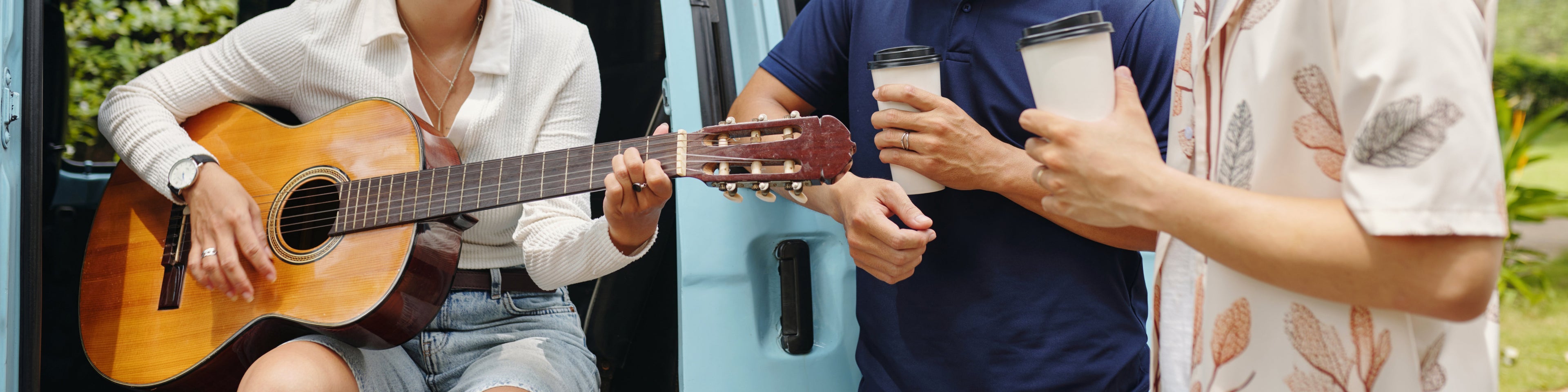 Person playing guitar with two others holding drinks outdoors