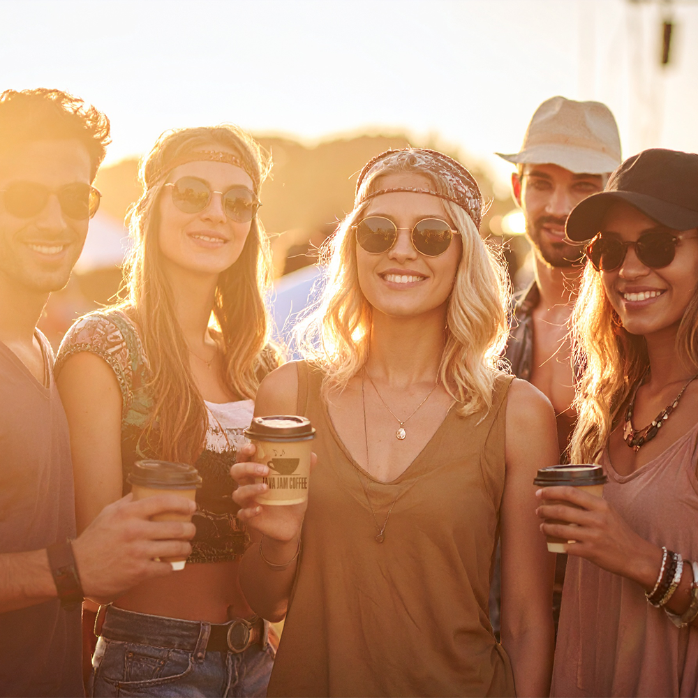 Group of friends at a music festival, holding coffee cups and smiling.