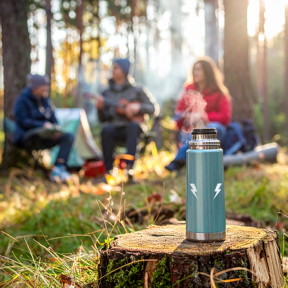 Teal insulated bottle on a stump with people camping in the background